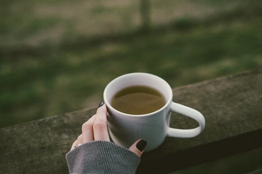 Closeup of a hand holding a mug of tea or coffee outdoors, capturing a serene morning moment.