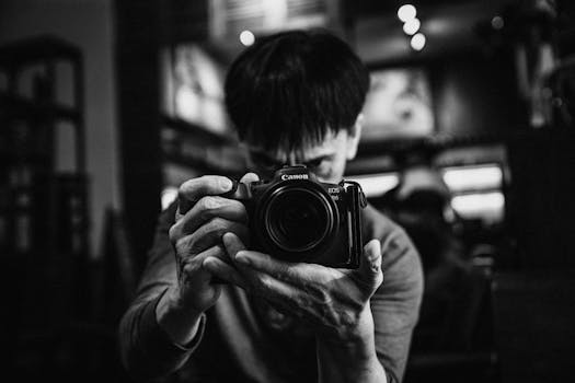 Artistic black and white portrait of a photographer capturing a moment indoors.