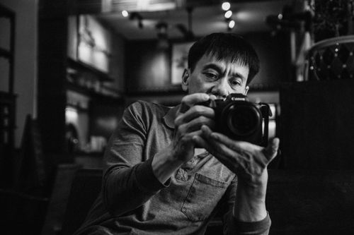 Free Monochrome portrait of a male photographer adjusting his camera in a cozy indoor setting. Stock Photo