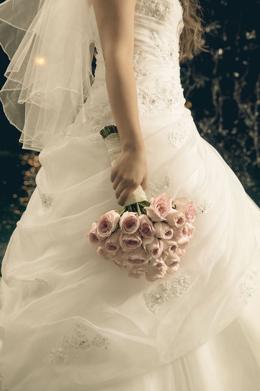 Stylish bride in an elegant gown holds a bouquet of pink roses, capturing a graceful wedding moment.