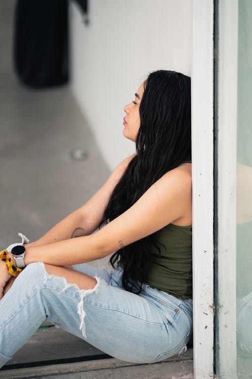 A woman sitting on the ground looking out the window