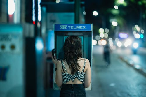 A woman standing in front of a pay phone at night