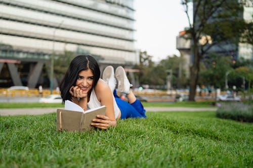 A woman is laying on the grass reading a book