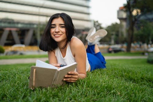 A young woman is laying on the grass reading a book