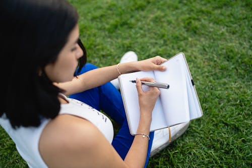A woman sitting on the grass writing in a notebook