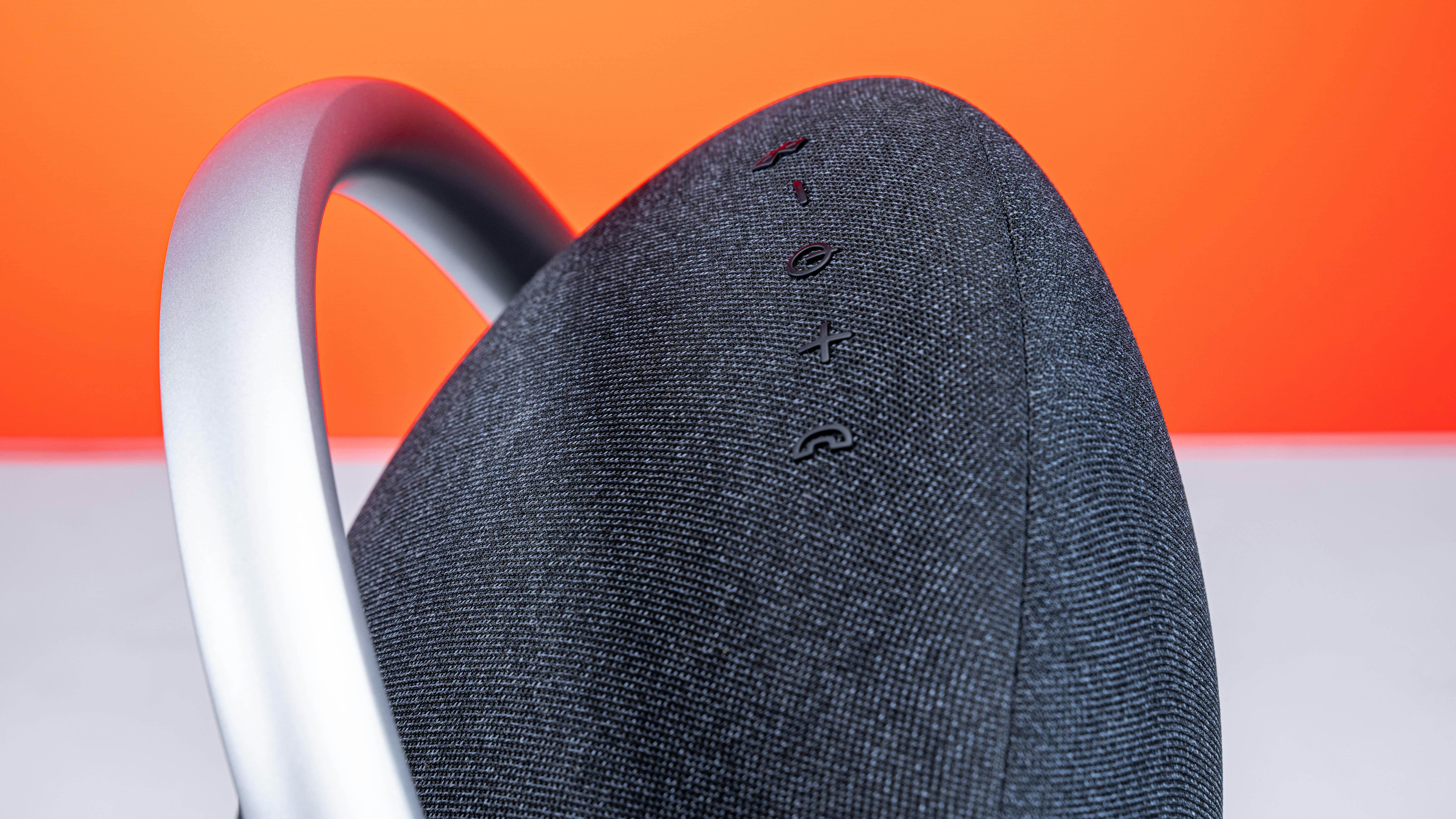 Close-up of a stylish wireless speaker with a handle against an orange background, emphasizing modern design.