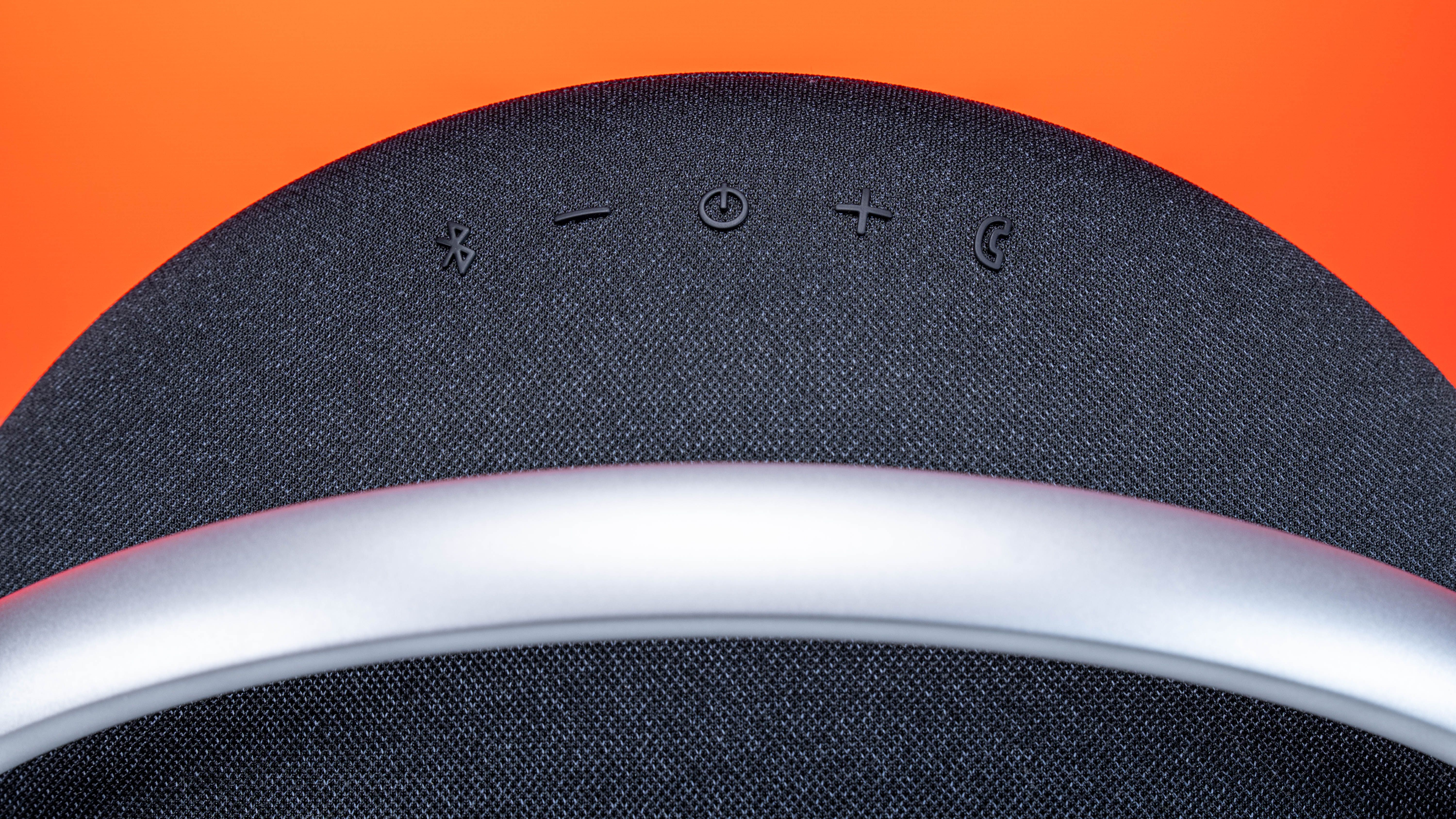 Close-up of a modern wireless speaker with an orange background, highlighting buttons and sleek design.
