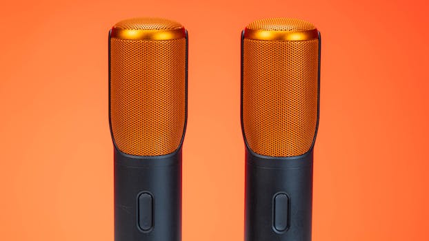 Vibrant photo of two modern microphones against an orange background, highlighting technology.