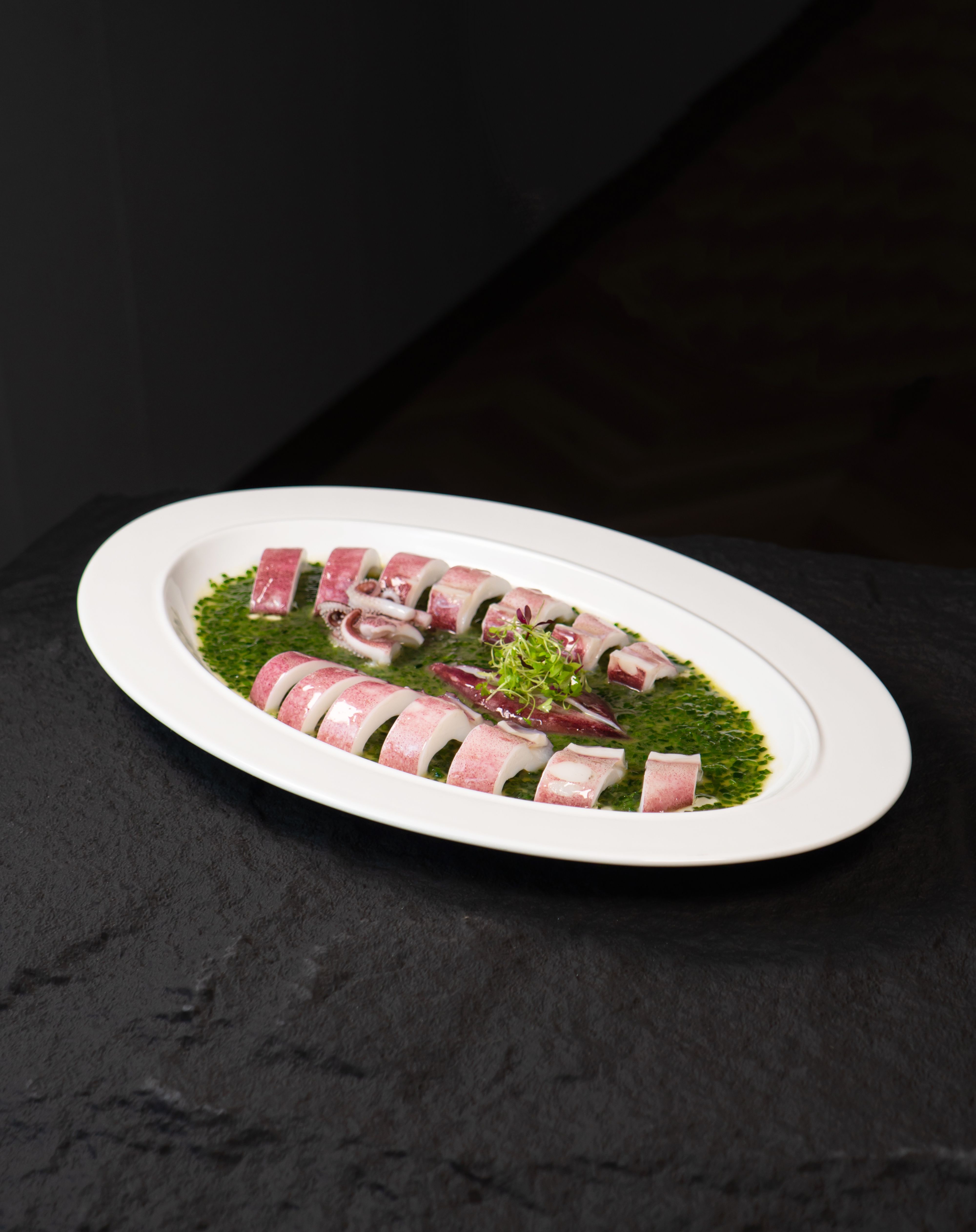Appetizing octopus slices on a plate with green herb sauce. Ideal for food presentations.