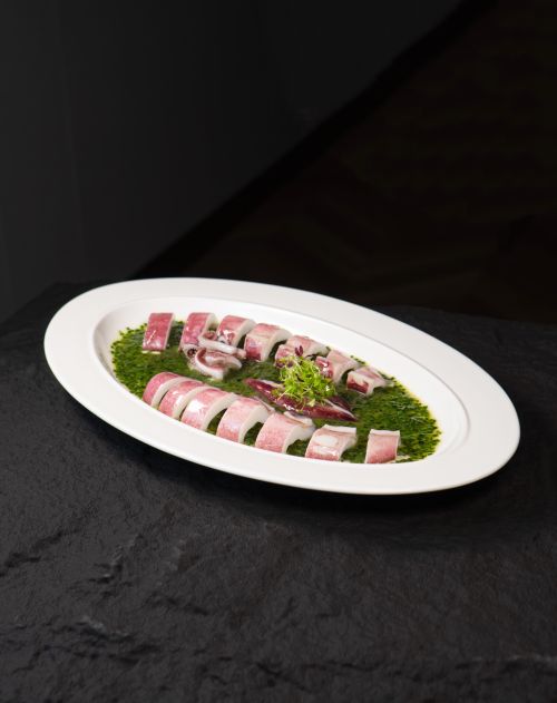 Free Appetizing octopus slices on a plate with green herb sauce. Ideal for food presentations. Stock Photo