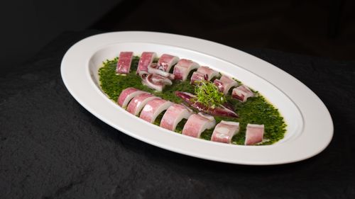 Free A beautifully presented octopus dish on a white plate with green sauce, ideal for gourmet food visuals. Stock Photo