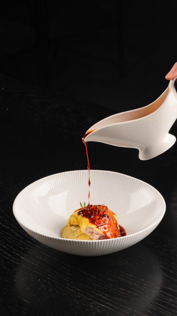 A white gravy boat filled with dark, speckled giblet gravy studded with chopped hard-boiled egg and minced giblets, next to a roasted turkey.