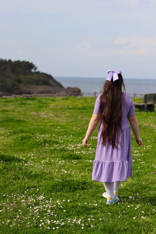 A little girl in a purple dress walking through a field