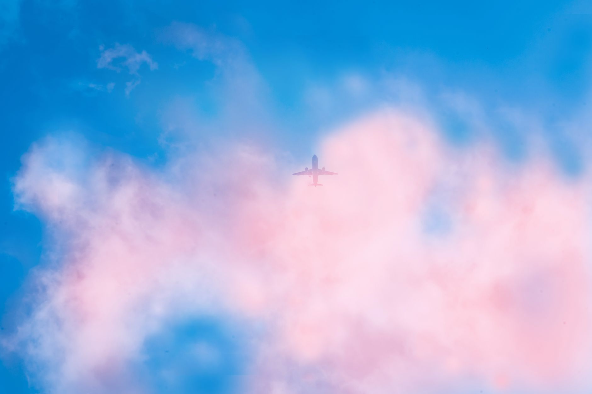 A single airplane soaring through vibrant pink and blue clouds, illustrating the beauty of aerial travel.