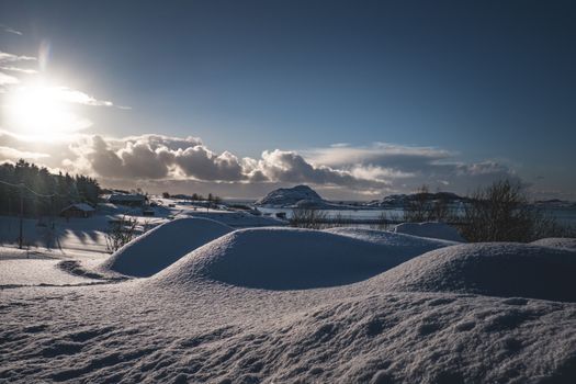 Calm winter landscape with snowy hills and a bright sun at sunset.