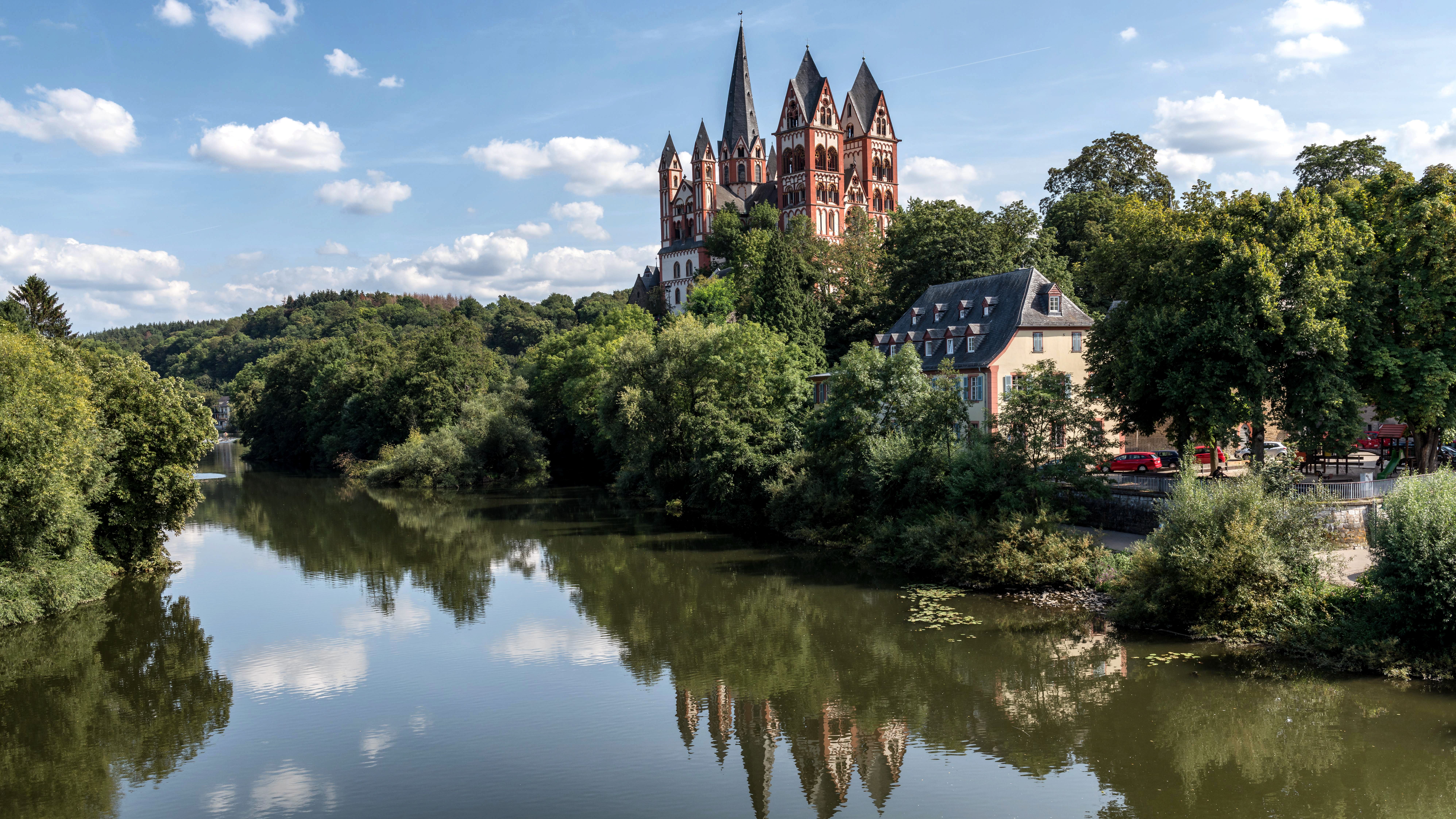 A scenic view of Limburg Cathedral overlooking the Lahn River, surrounded by lush greenery.