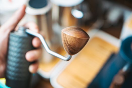 Detailed view of a manual coffee grinder with wooden handle in hand.