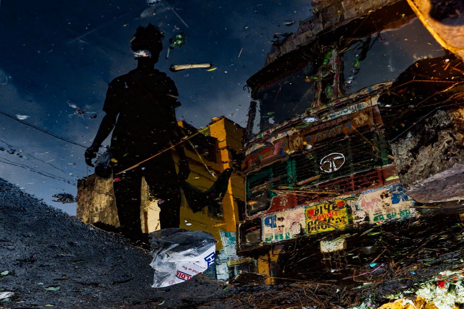 A striking reflection of a silhouette and truck in a water puddle in Kolkata at night.