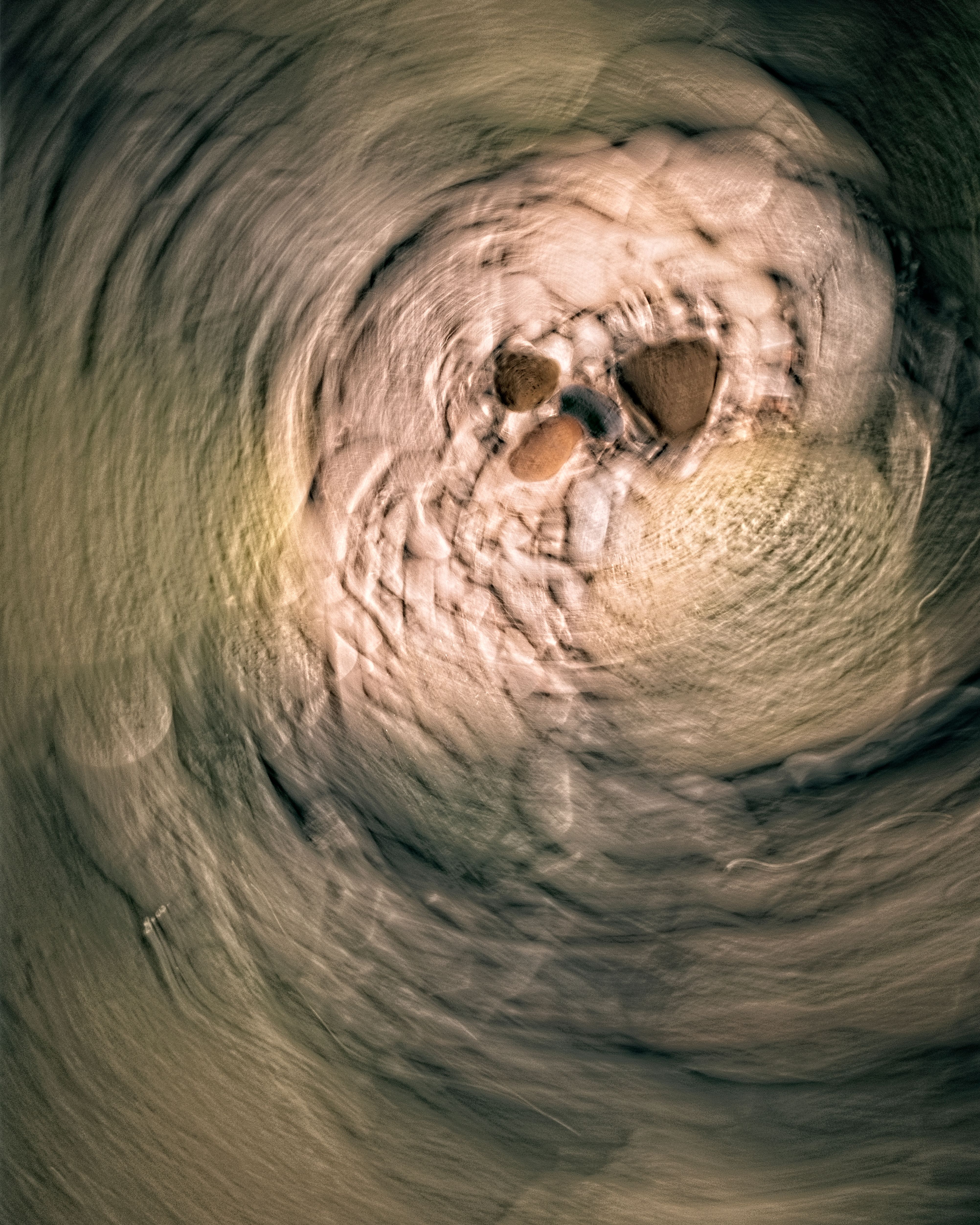 Abstract image of pebbles creating a swirling pattern in a riverbed, depicting earth tones and tranquil motion.