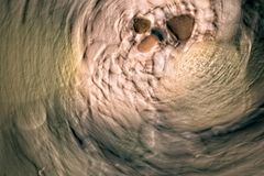 Abstract image of pebbles creating a swirling pattern in a riverbed, depicting earth tones and tranquil motion.