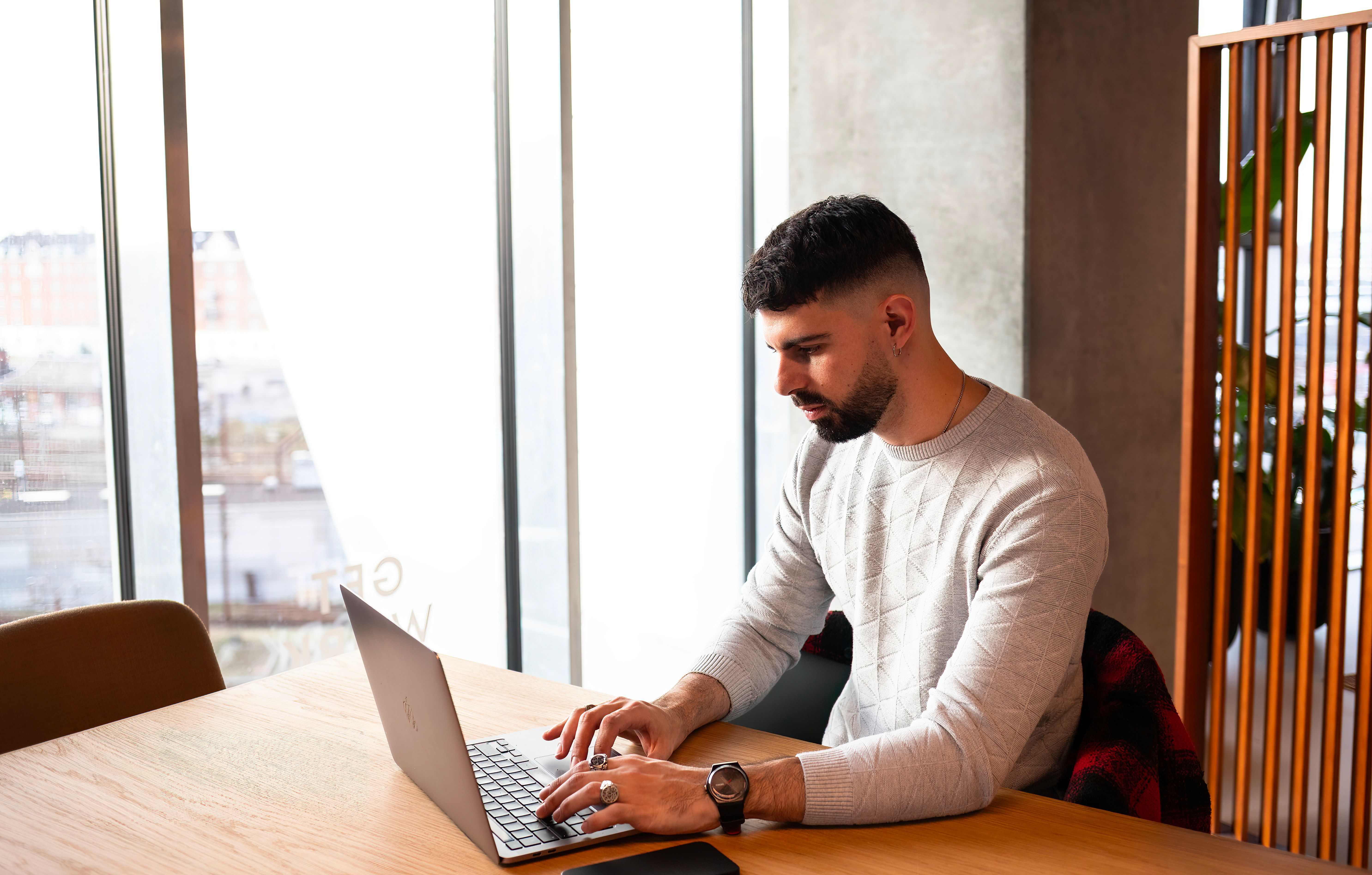 Man with beard typing on laptop indoors in a modern office setting in Copenhagen.