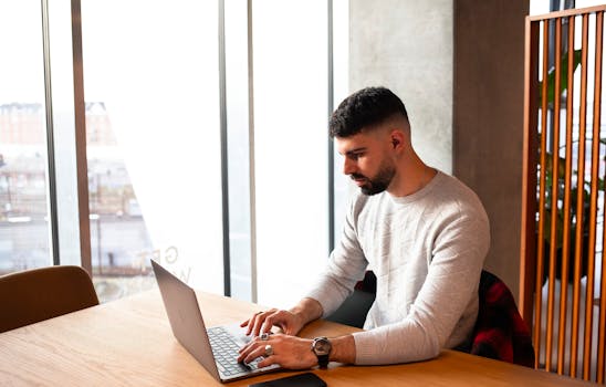Man with beard typing on laptop indoors in a modern office setting in Copenhagen.