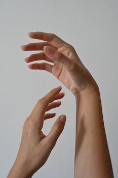 A minimalist close-up of female hands gracefully posed against a neutral background.
