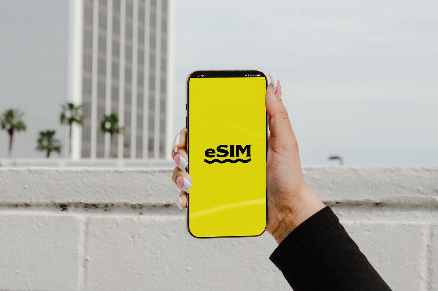 A hand holding a smartphone displaying the word eSIM against an urban skyline
