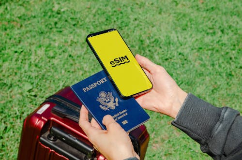 Una Mano Che Tiene Sia Un Passaporto Che Un Telefono Con E Sim, Che Indica Le Moderne Necessità Per I Viaggi Internazionali.