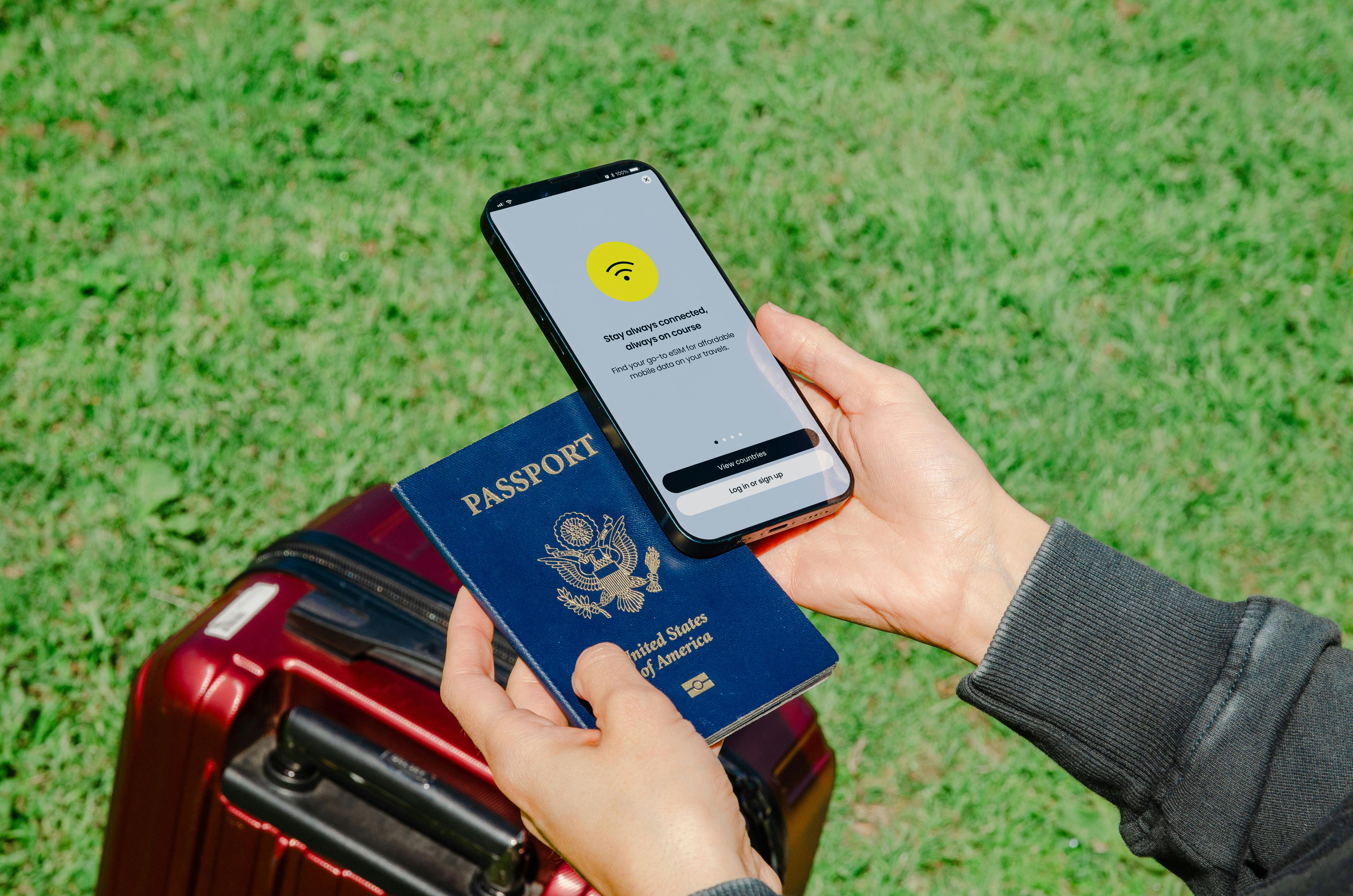 Close-up of hands holding a passport and smartphone with lost connection outdoors beside luggage.