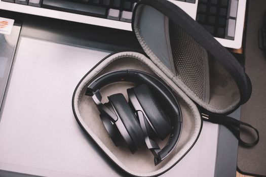Compact black wireless headphones stored in a protective case placed on a desk, showcasing modern technology.