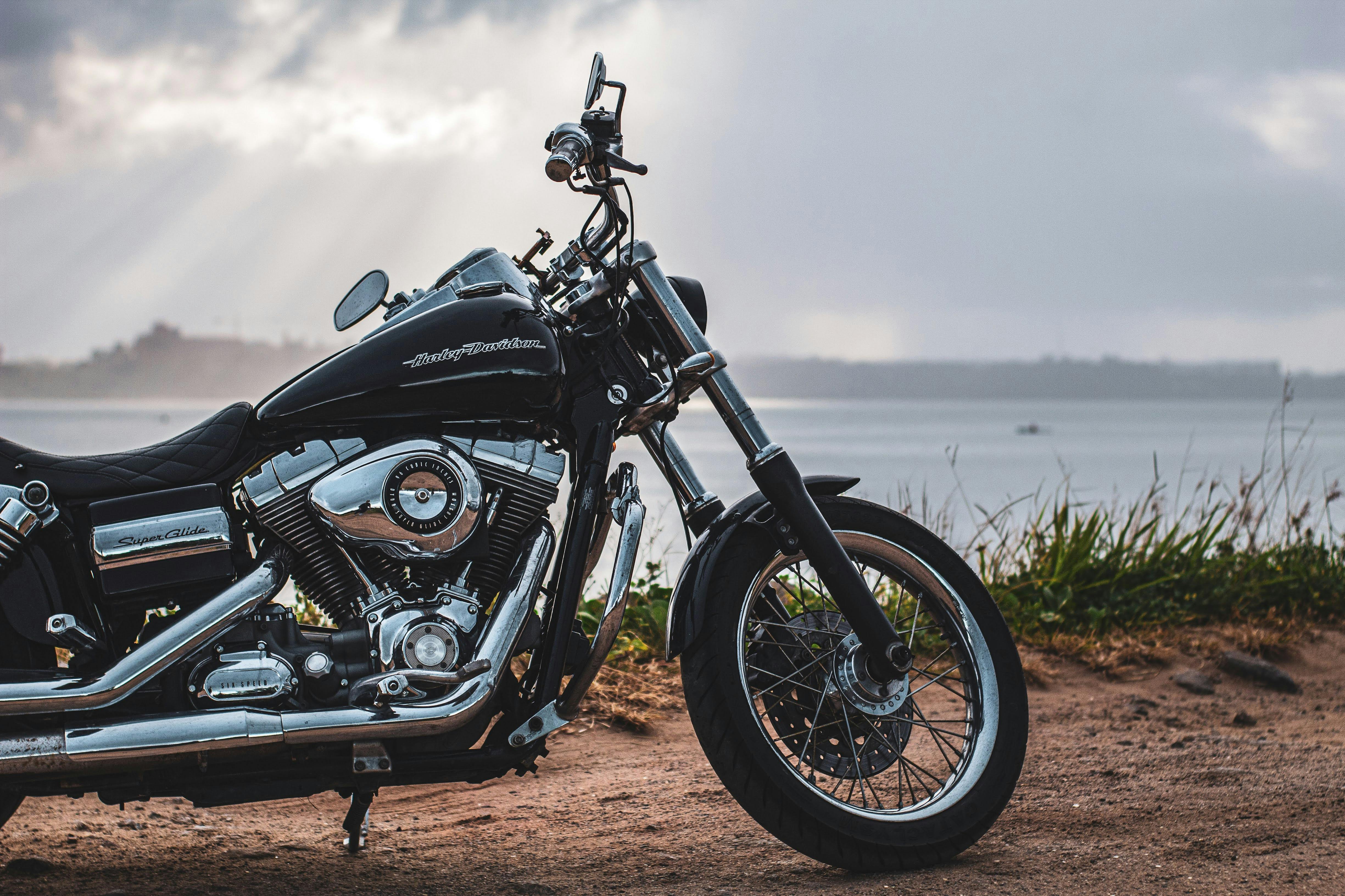 A classic black Harley Davidson motorcycle parked on a rural lakeshore road during sunset.