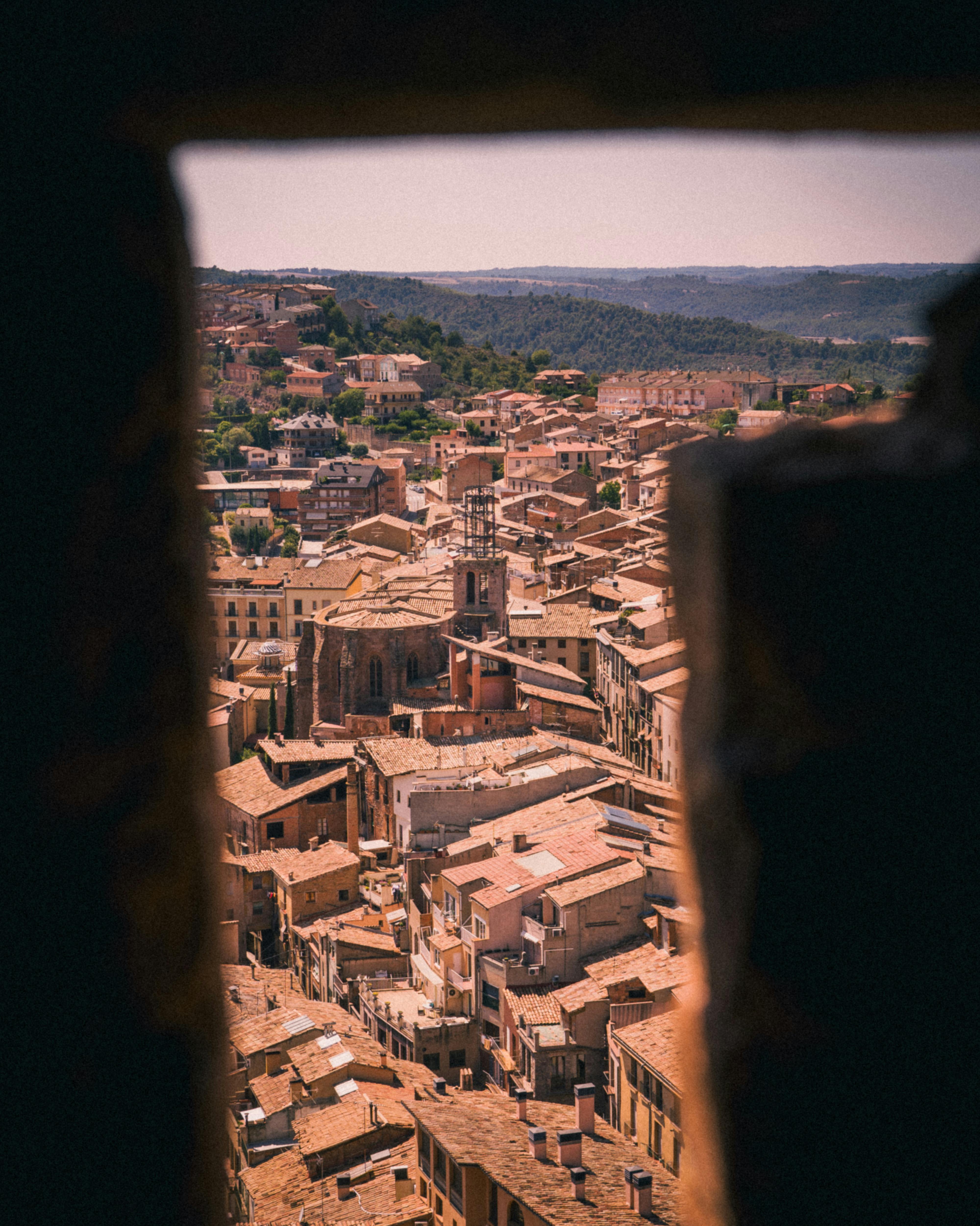 A picturesque view of Berga, Spain from a stone archway, showcasing the warm summer townscape.