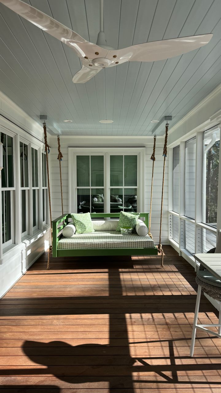 Side patio design with a small wooden porch swing hanging from a freestanding frame next to a fence
