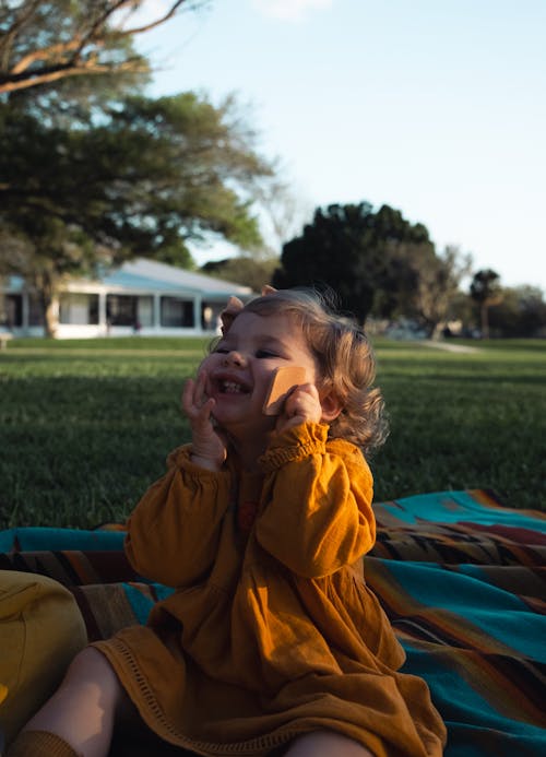 A toddler sitting on a blanket in the grass