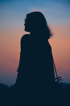 Silhouette of a woman with glasses against a vibrant twilight sky, creating a peaceful sunset scene.