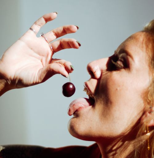 Free A close-up shot of a woman joyfully eating a cherry, emphasizing playfulness and taste. Stock Photo