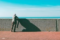 一位老人倚在海边的墙上，欣赏着阳光明媚、风景优美的海景