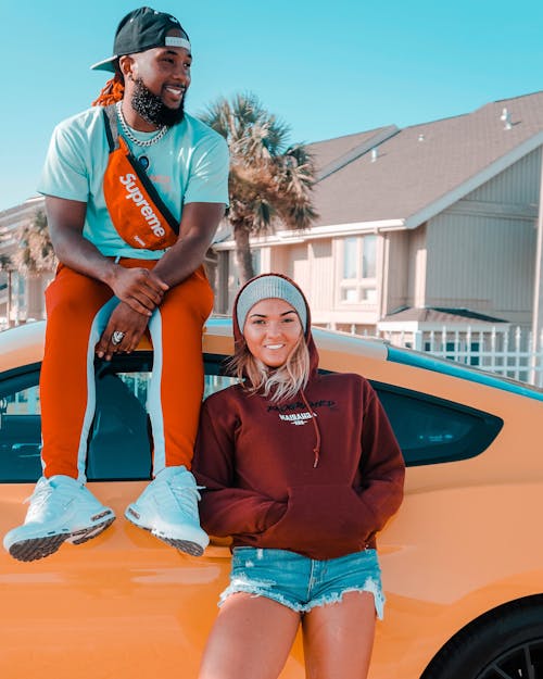 Man Wearing White Crew-neck Shirt and Orange Track Pants Sitting on Top of Luxury Car