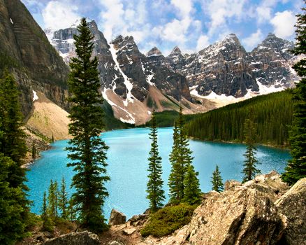 Beautiful view of Moraine Lake with turquoise waters surrounded by snow-capped Rocky Mountains and evergreen trees.
