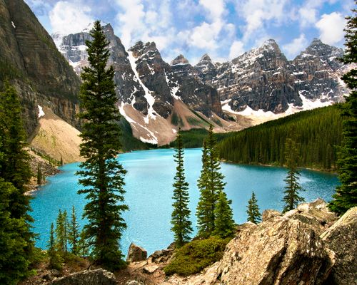 Free Beautiful view of Moraine Lake with turquoise waters surrounded by snow-capped Rocky Mountains and evergreen trees. Stock Photo