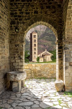 Beautiful view of a Romanesque church and bell tower through stone archway in Bohí, Spain.