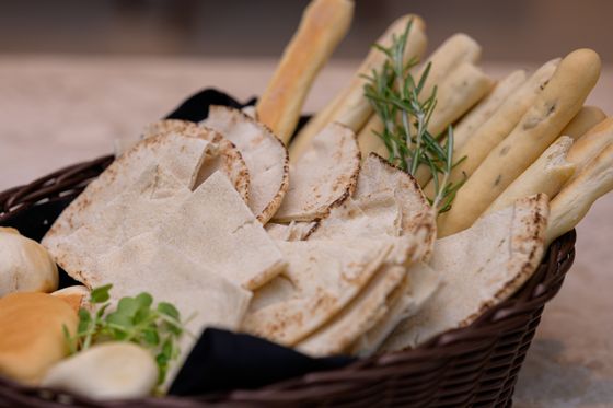 Wicker basket with pita triangles, long breadsticks, soft rolls, rosemary sprigs and fresh herbs