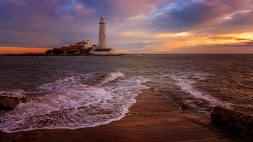 Free A stunning view of St Mary's Lighthouse at sunset with dramatic skies and ocean waves. Stock Photo