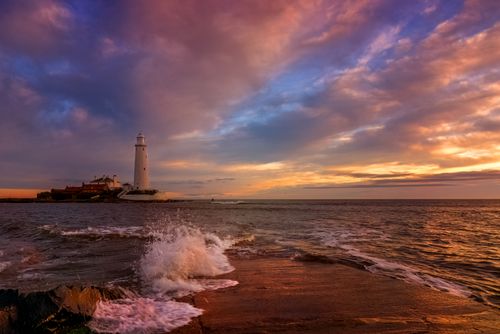 Free Breathtaking sunset view of St Mary's Lighthouse with crashing waves at the UK coast. Stock Photo