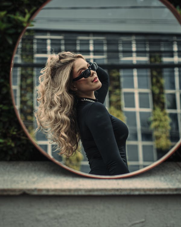 A woman with long blonde hair is looking in a mirror
