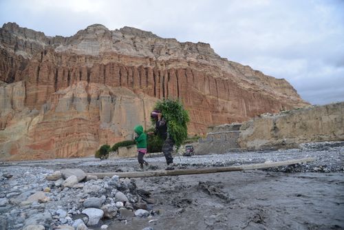 Free A mother and child walk across a rocky landscape in Upper Mustang, Nepal with a steep cliff backdrop. Stock Photo