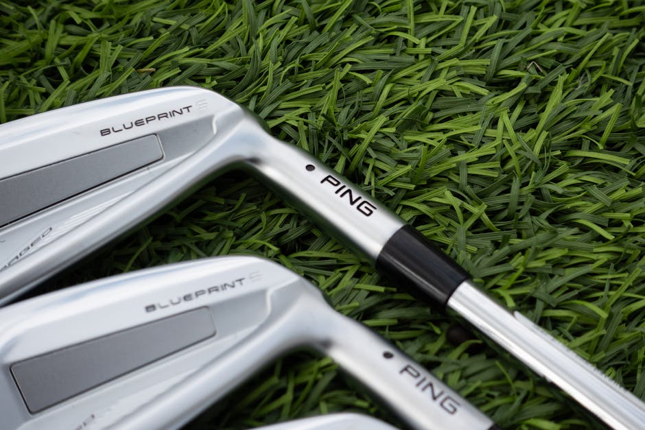 Detailed view of silver golf clubs resting on lush green grass, perfect for sports enthusiasts.