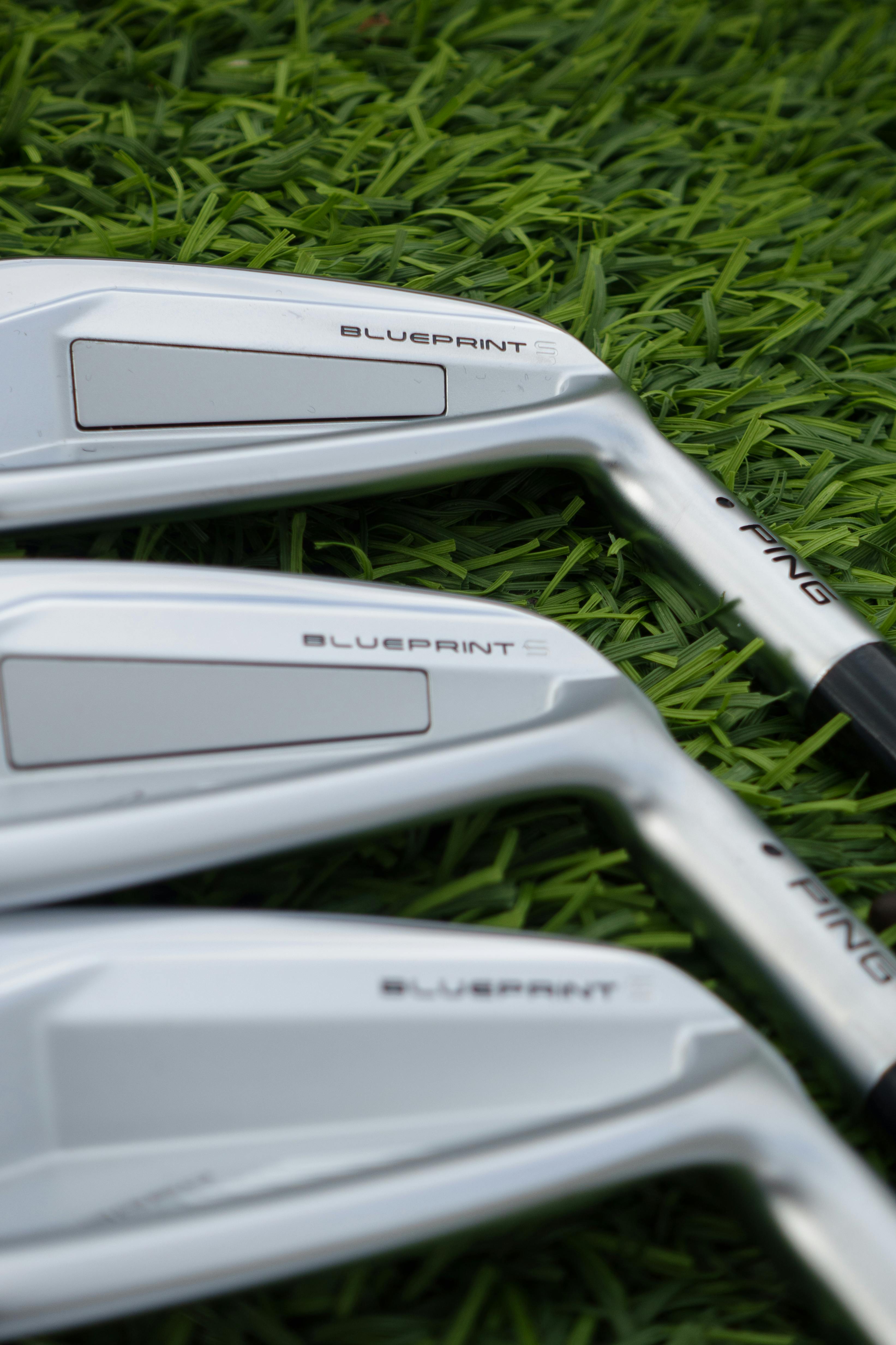 Detailed view of silver golf clubs resting on vibrant green grass, ideal for golf-related content.