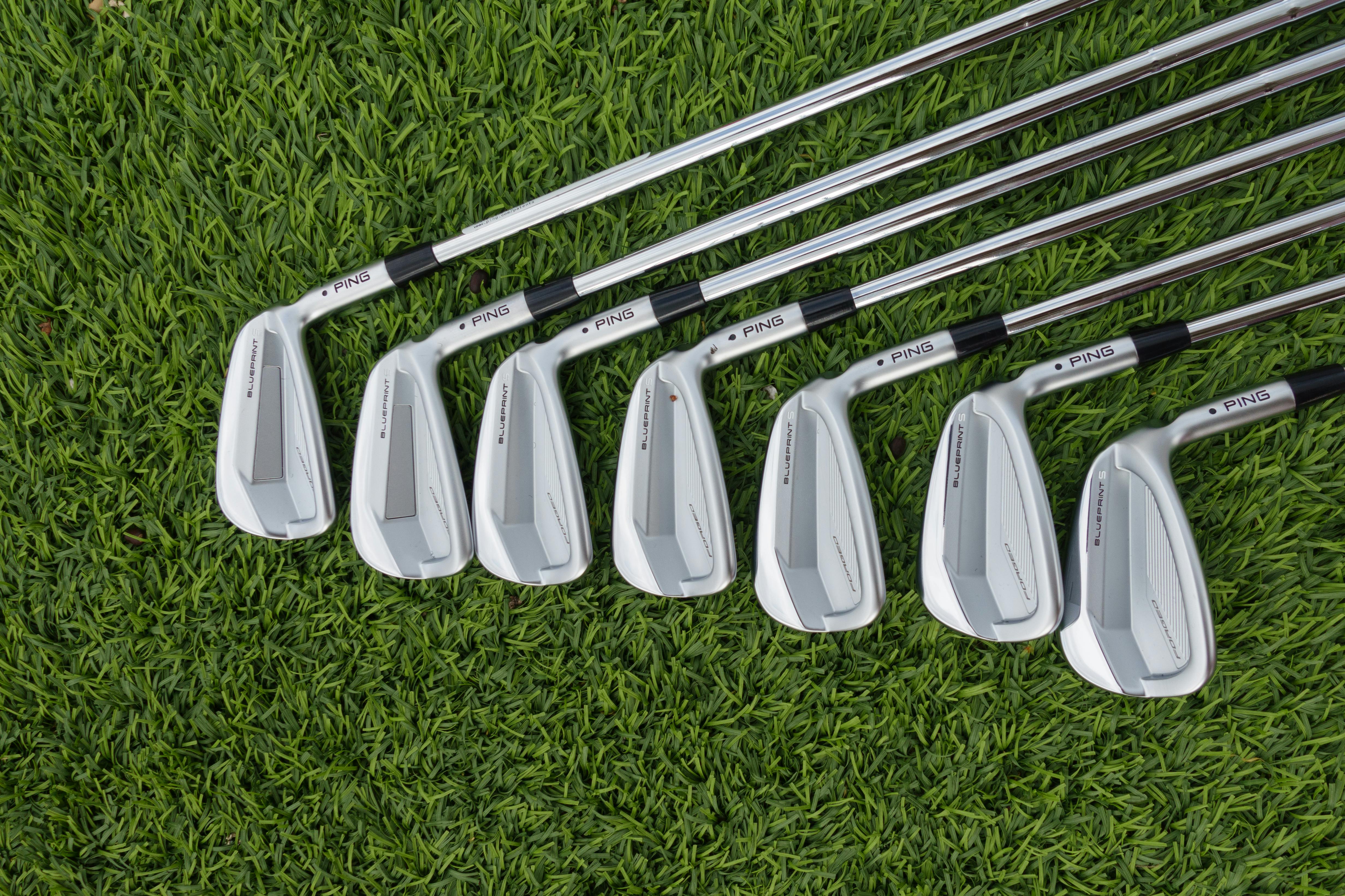 Top view of a set of sleek modern golf clubs arranged on vibrant green grass.